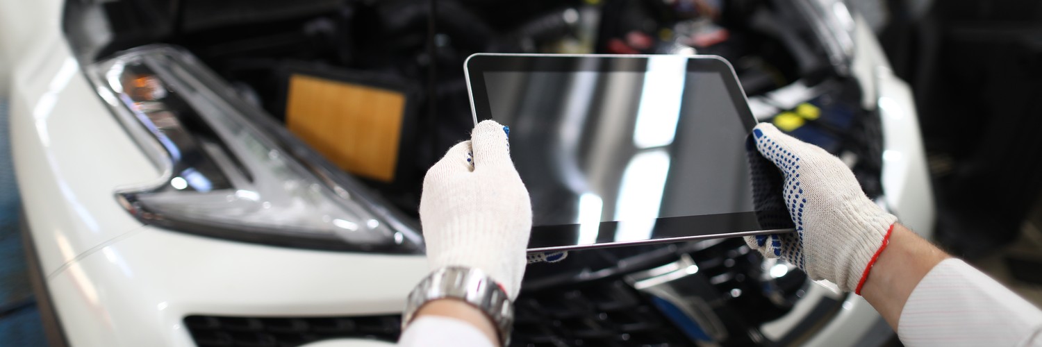 Manos con guantes sujetan una tableta de diagnóstico frente a un coche