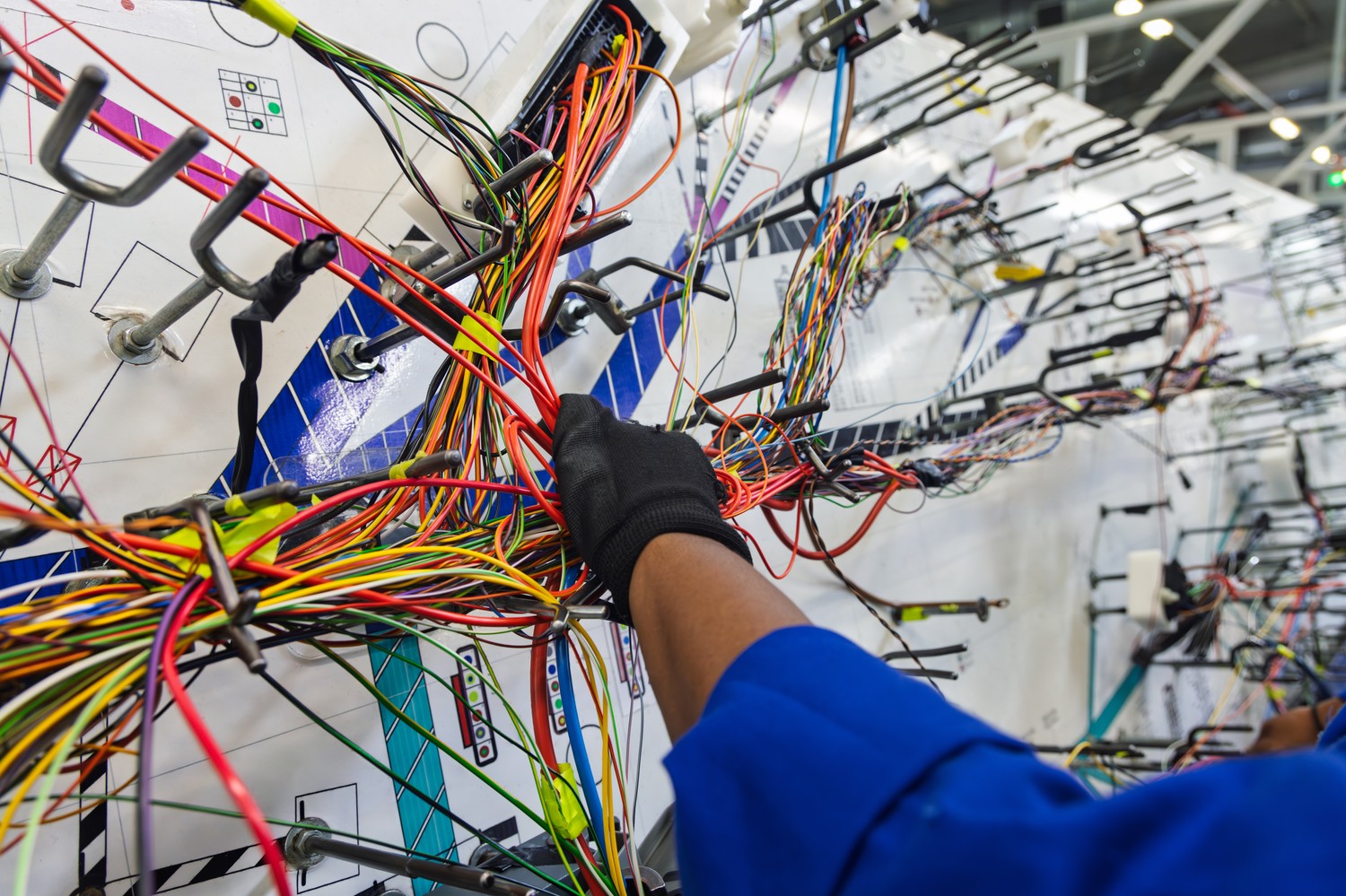 Manos con guantes conectando un mazo de cables sobre un tablero