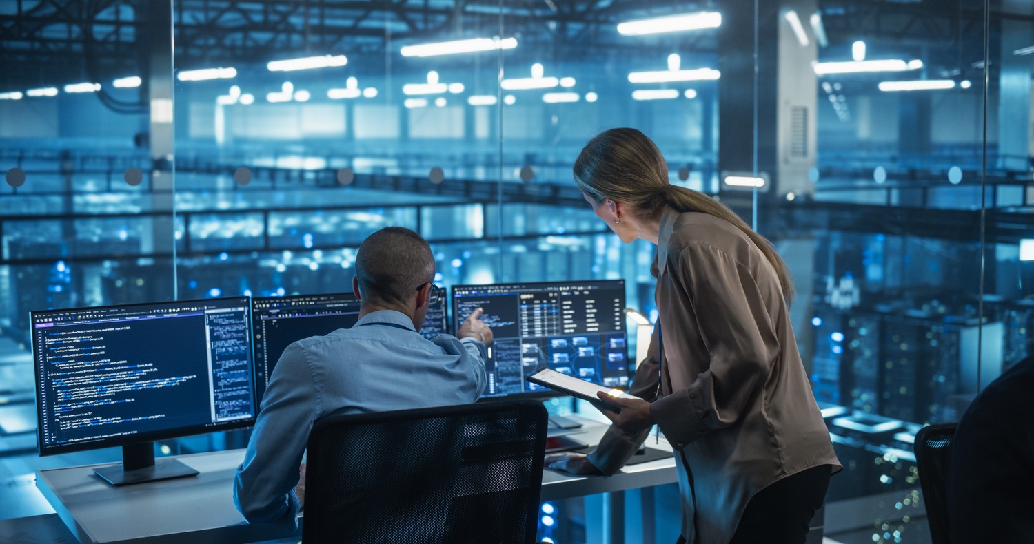 Technicians monitoring systems in a control room with multiple screens