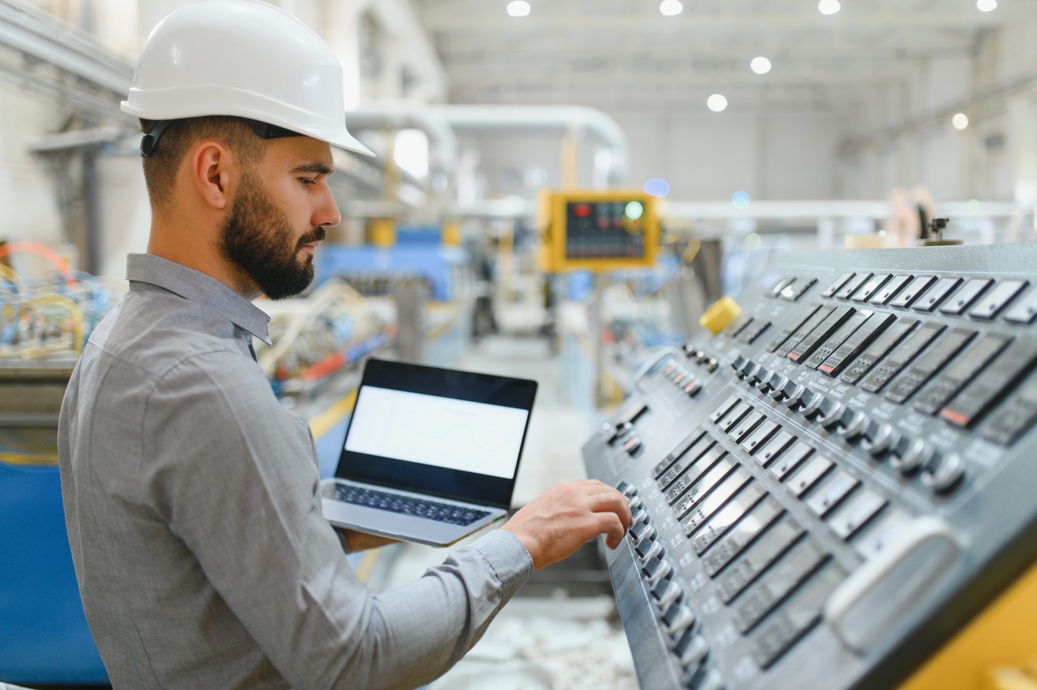Ingeniero con portátil manejando un panel de control en planta