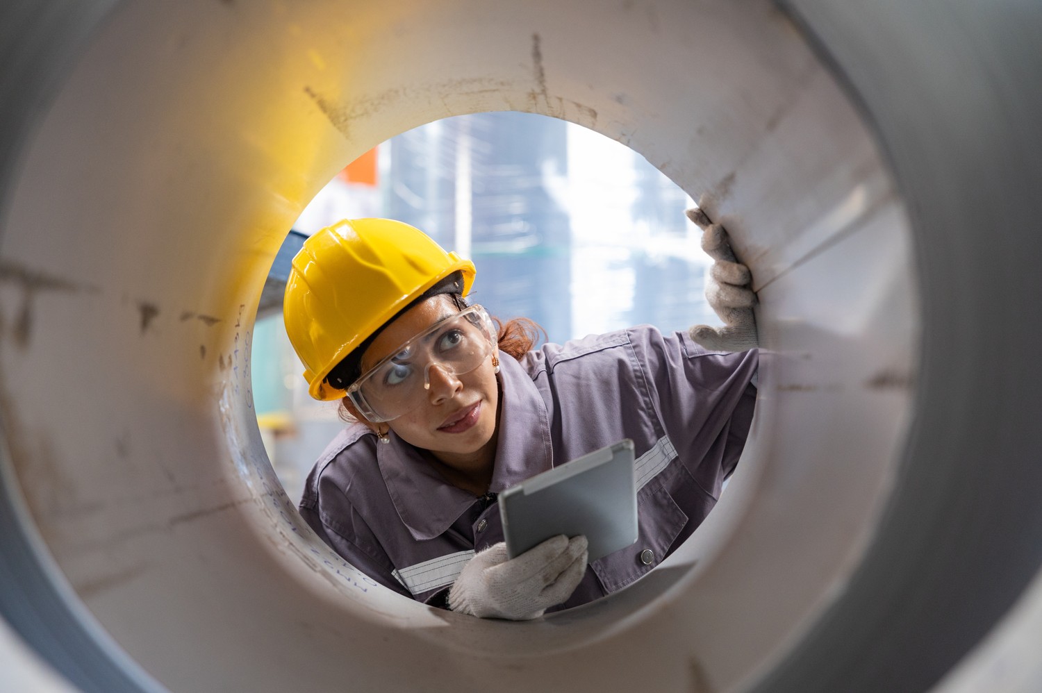 Ingeniera con casco inspeccionando el interior de un gran tubo de acero con una tableta
