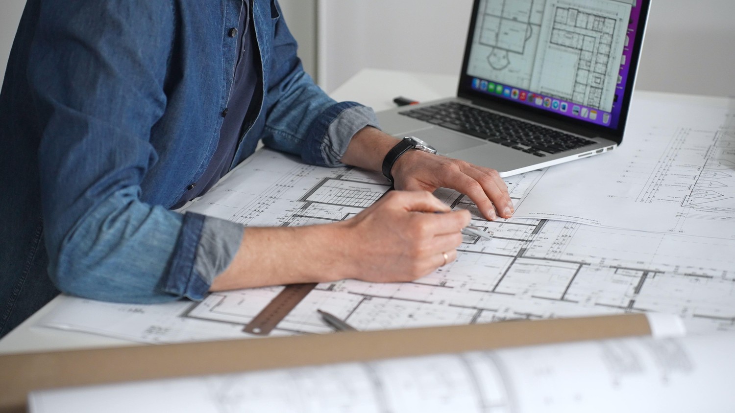Arquitecto revisando planos de planta sobre la mesa junto a un portátil