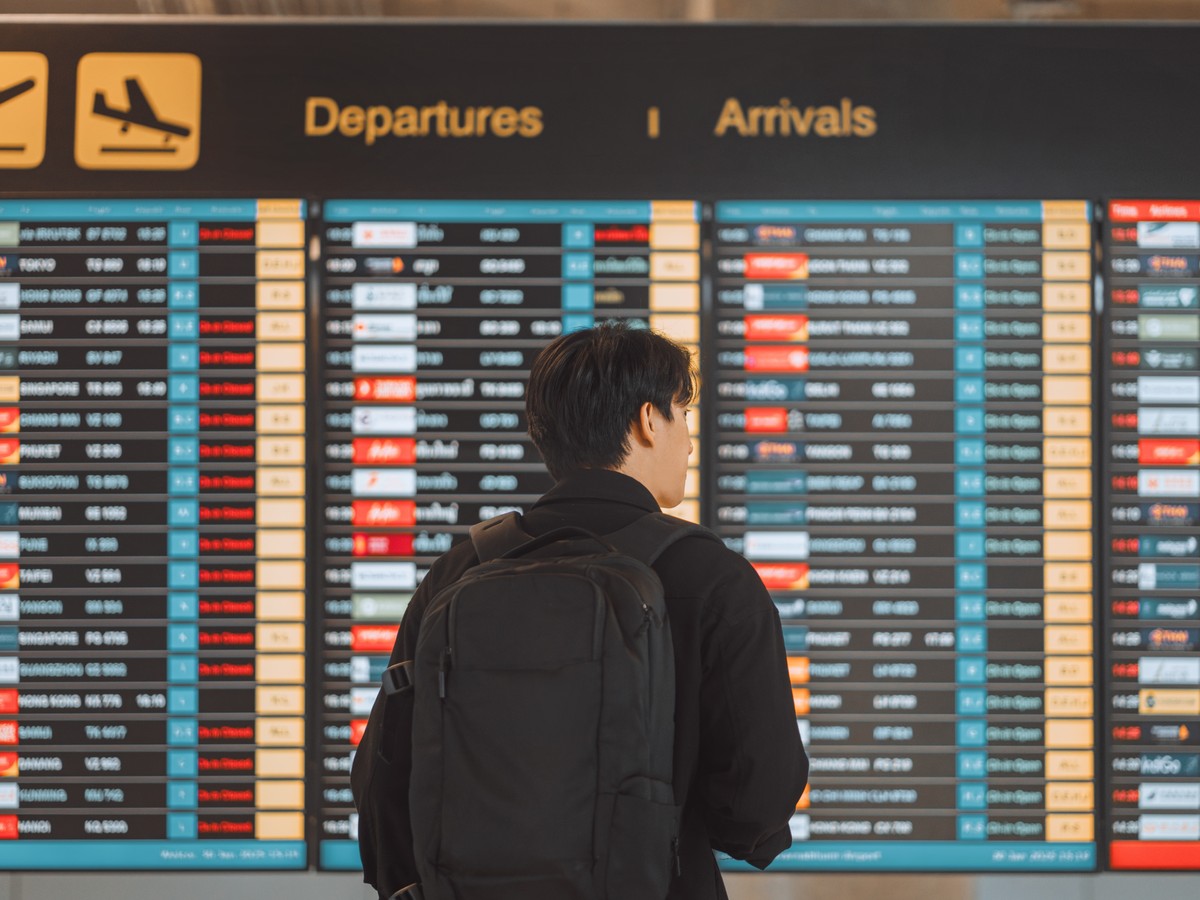 Una persona con mochila consulta el panel de salidas de un aeropuerto