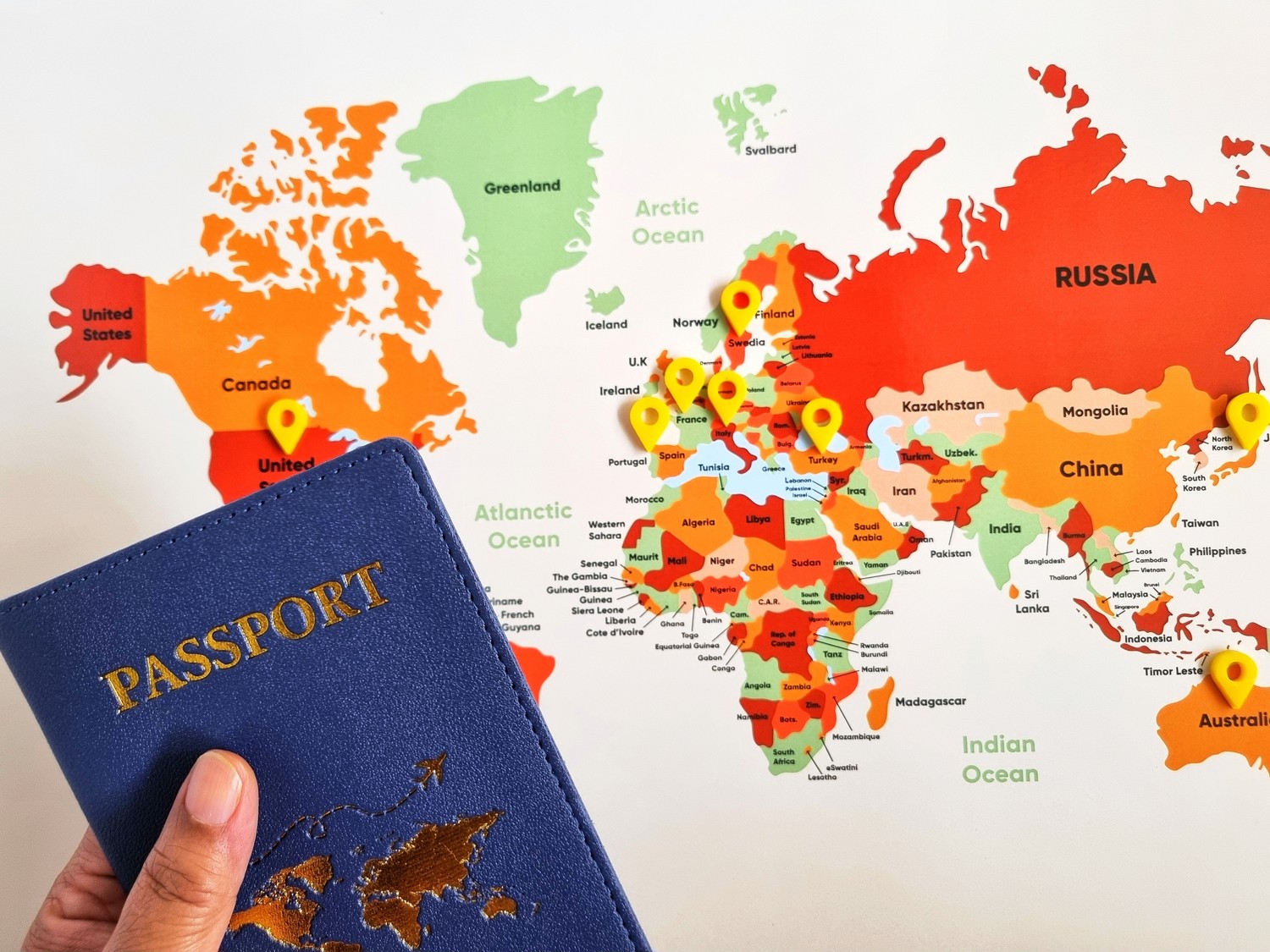Mano sosteniendo un pasaporte delante de un mapa del mundo con marcadores