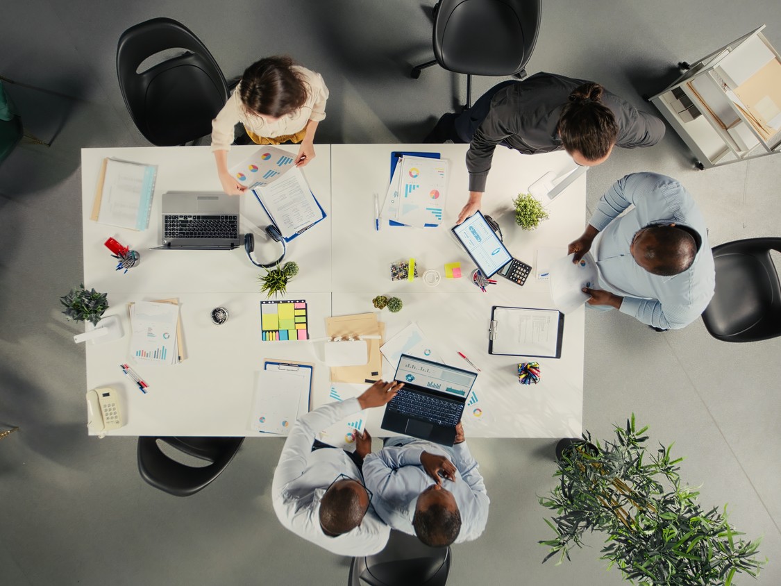 Vista cenital de un equipo revisando datos y propuestas alrededor de una mesa