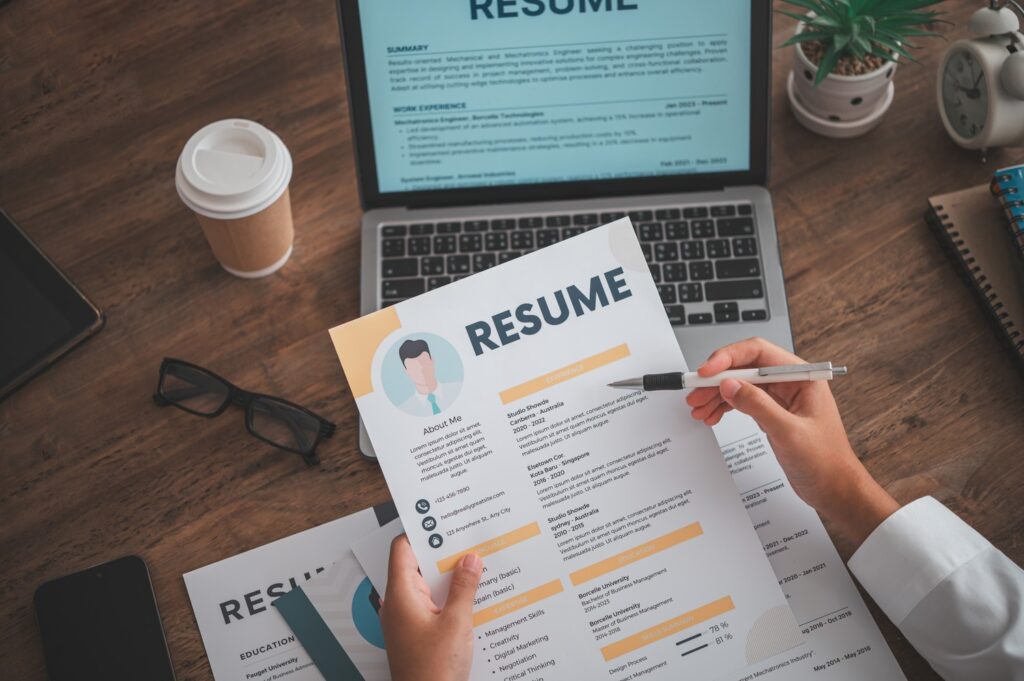 Persona revisando un currículum en papel junto a un portátil sobre una mesa